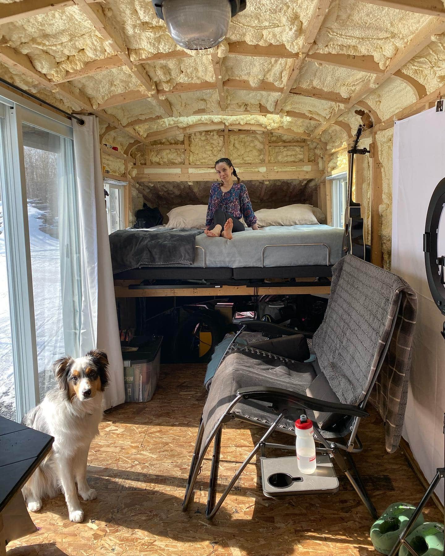 Not a Regular Skoolie's Gabi sitting on the bed in their skoolie while their dog sits on the floor