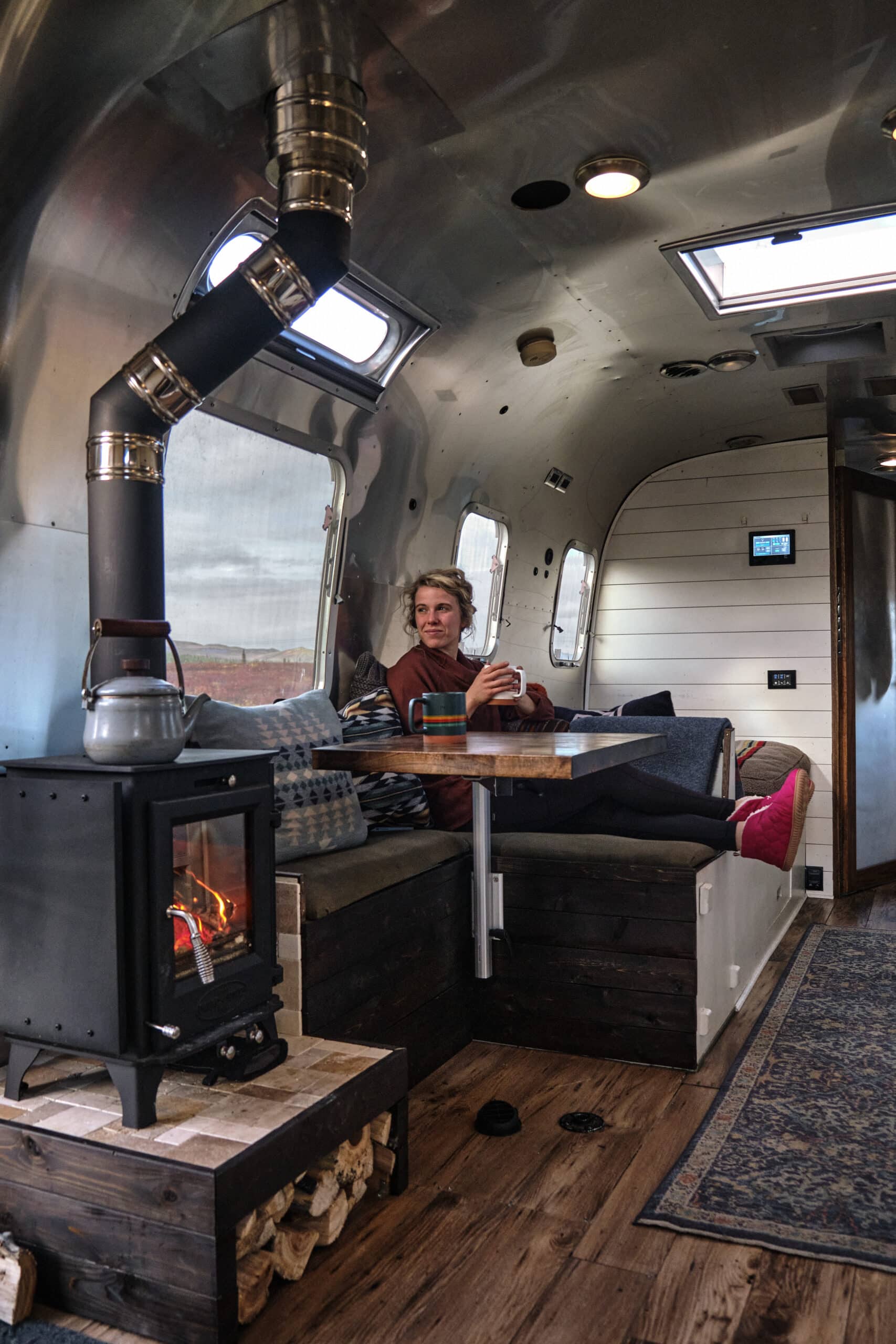 Kendall Strachan in the Living Area of Her Renovated Airstream with Wood Burning Stove Going