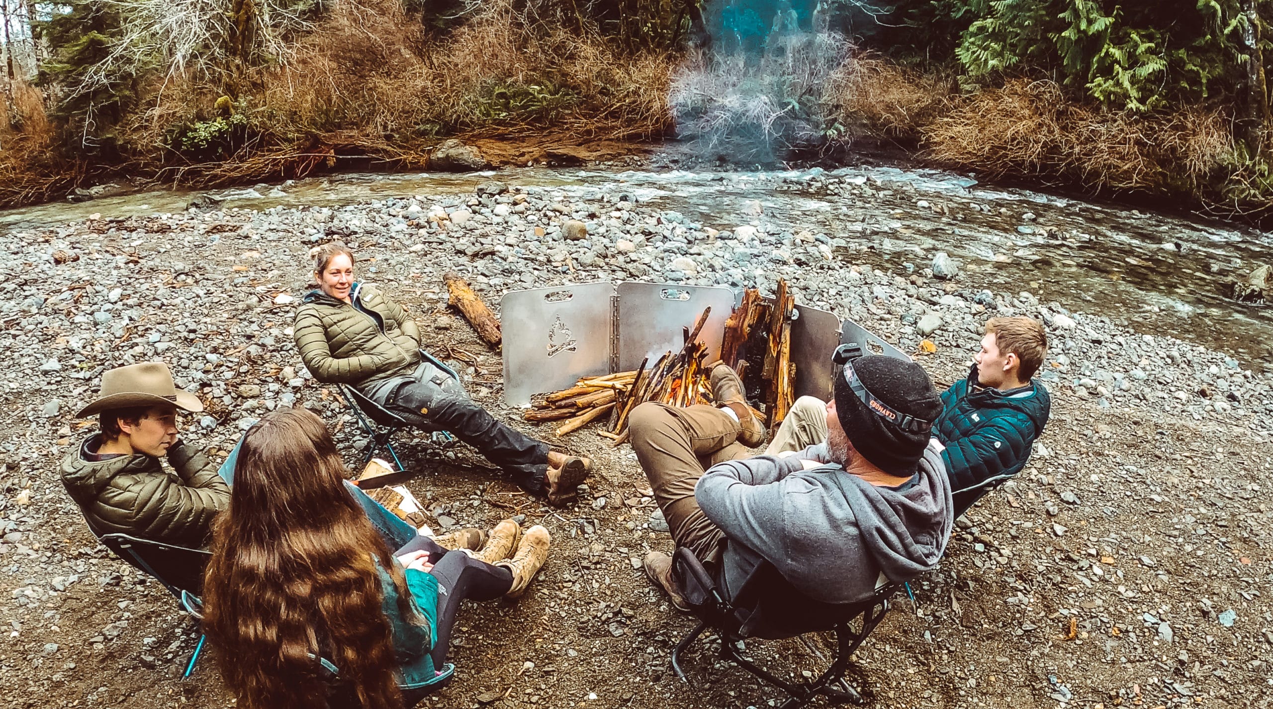 van Stralen Family sitting around a campfire next to a creek