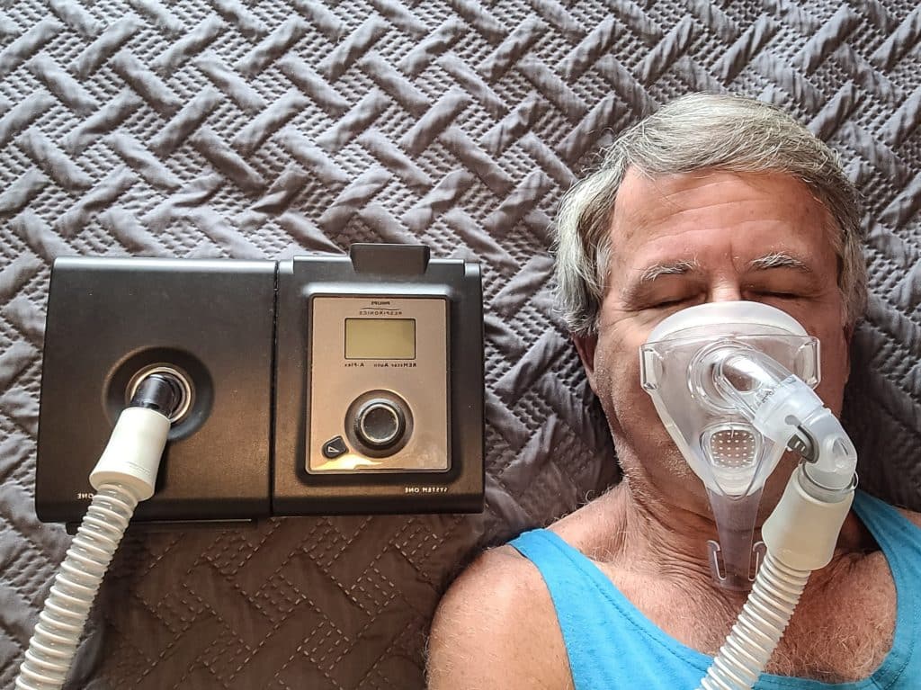 Man wearing CPAP mask laying next to a CPAP machine