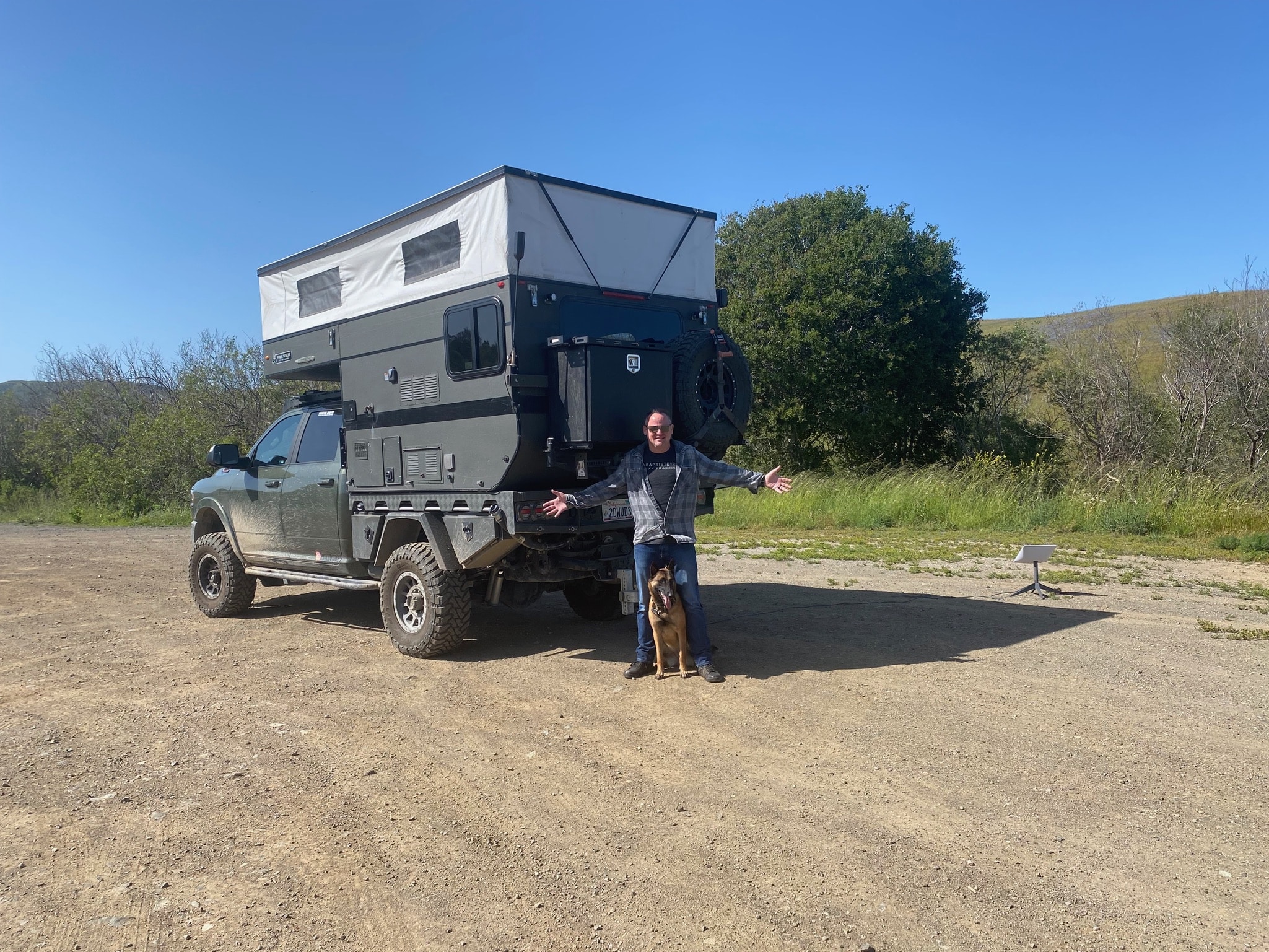 Sean Silvera with his dog posing with his arms open in front of his overlanding rig