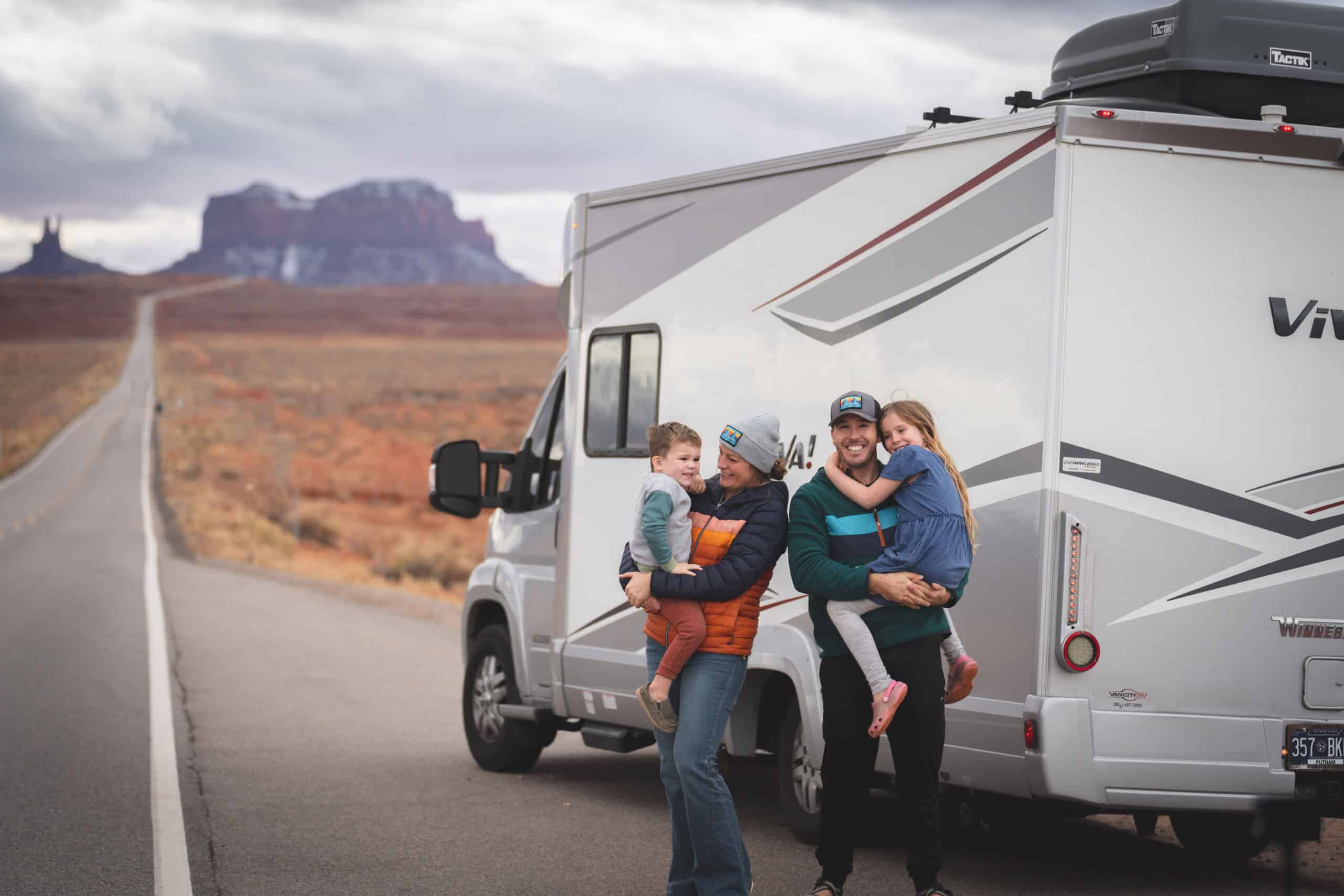 Less Junk More Journey holding their kids outside of their parked Winnebago