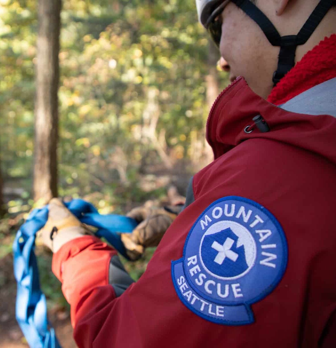 Seattle Mountain Rescue over the shoulder shot off a man with gloves tying a rope