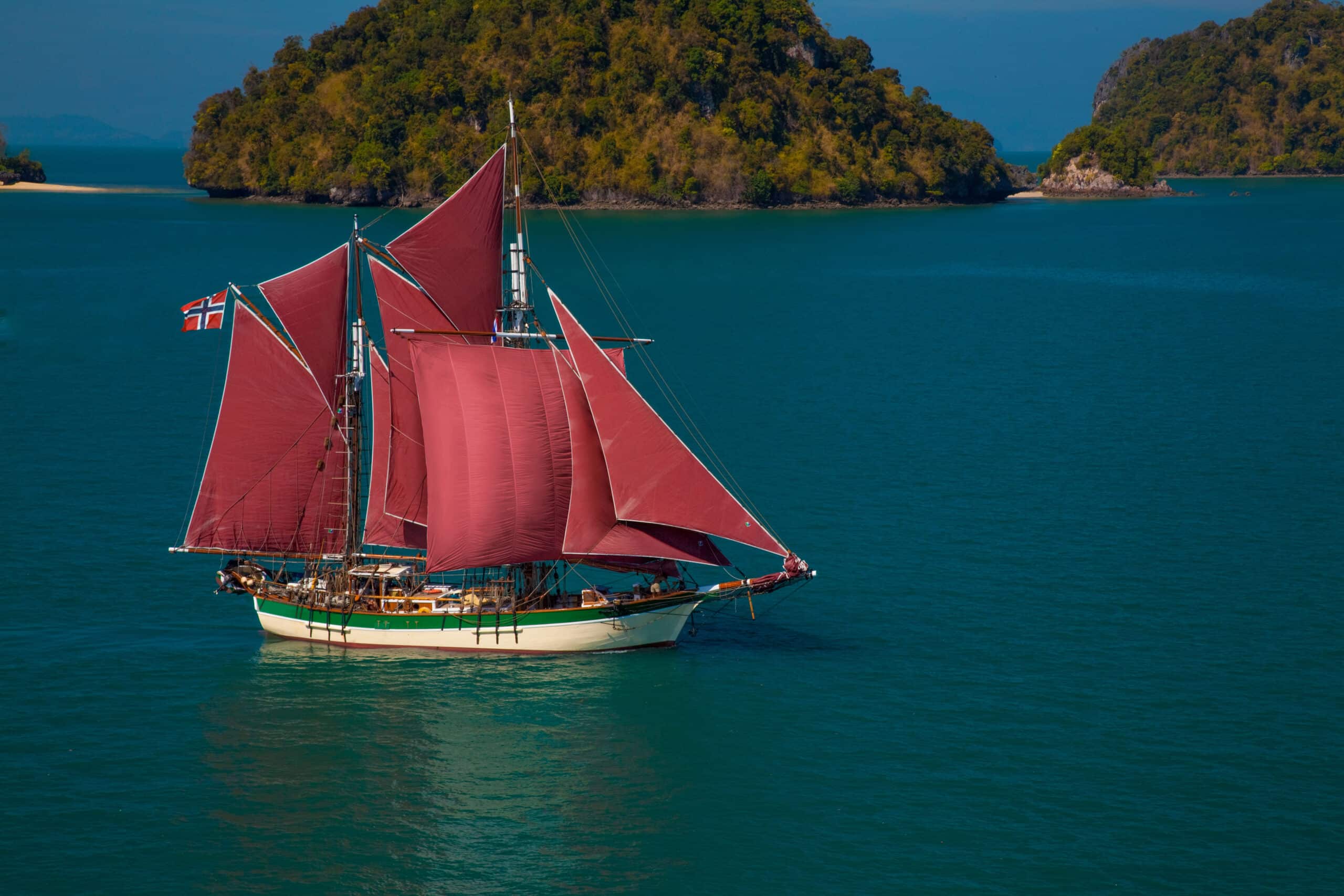 A sailboat sails through turquoise waters with red sails, powered by lithium batteries