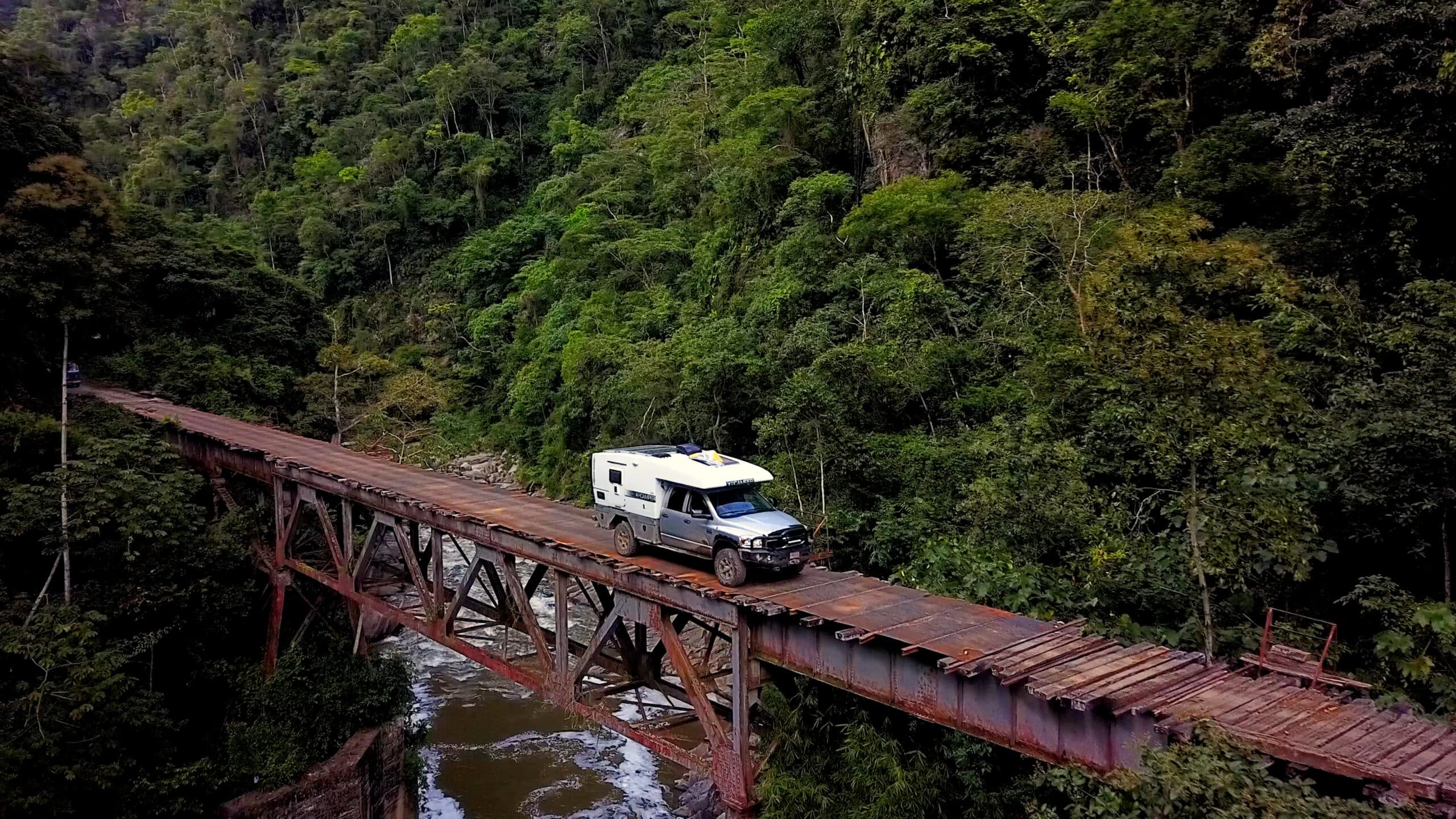 A Nimble overlanding truck is driving over a bridge in the forest.