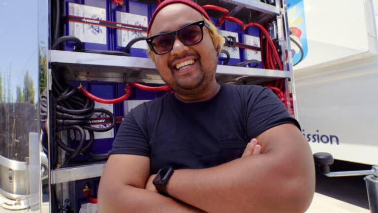 Pari is standing with his arms crossed and smiling in front of his Battle Born Batteries.
