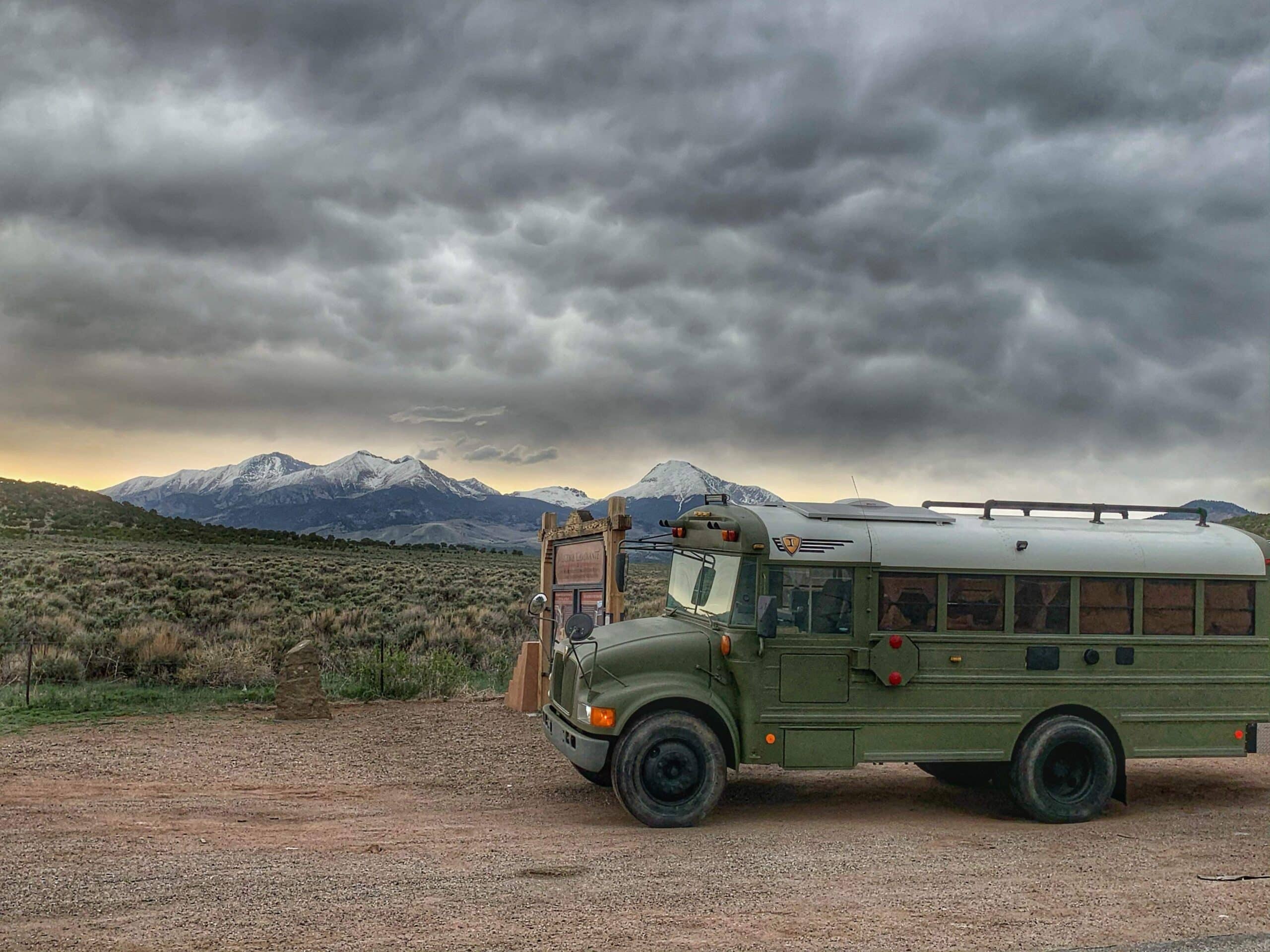A green skoolie is boondocking next to the "Welcome Camininante" sign