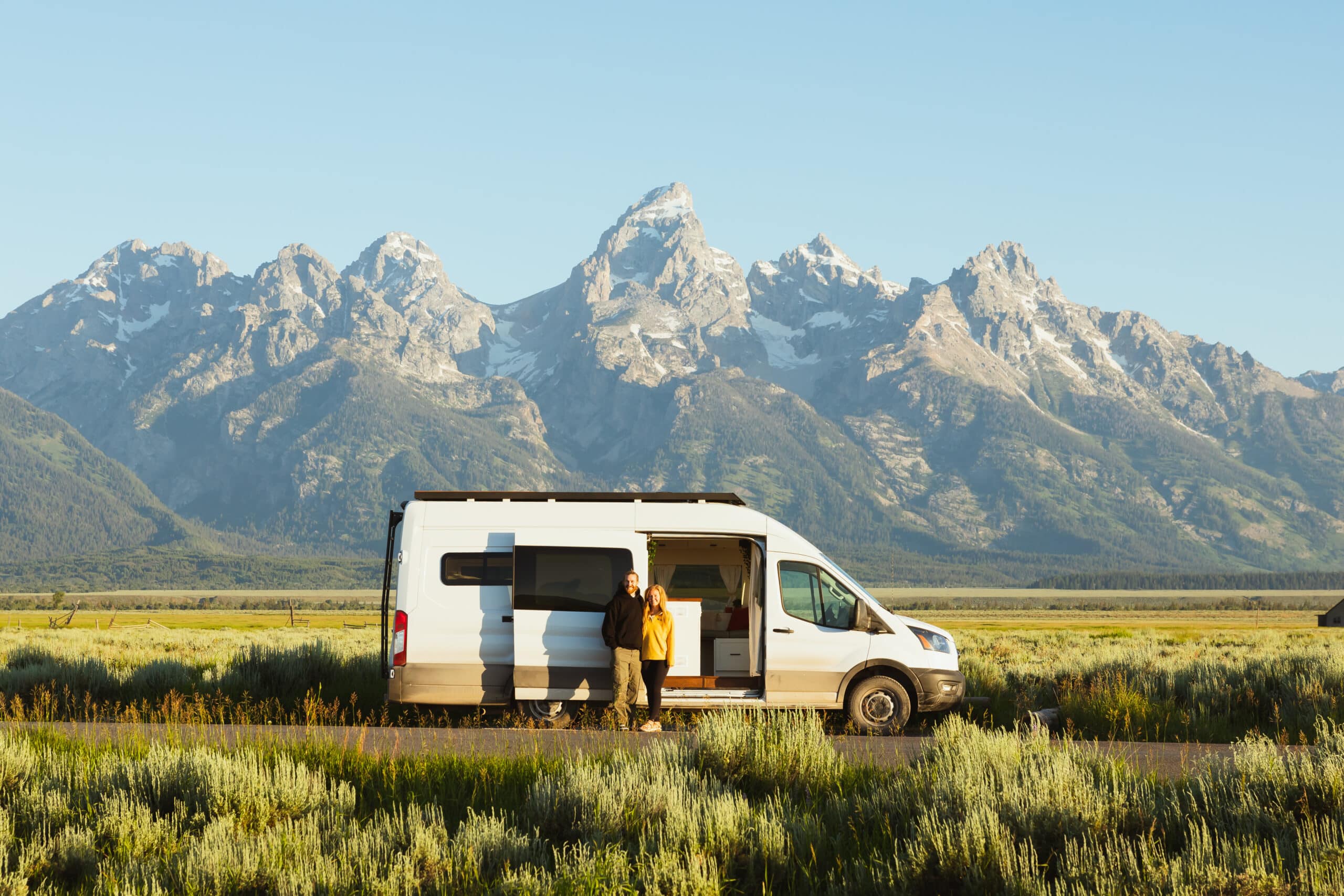 Couple poses in front of their van in front of the Rocky Mountains