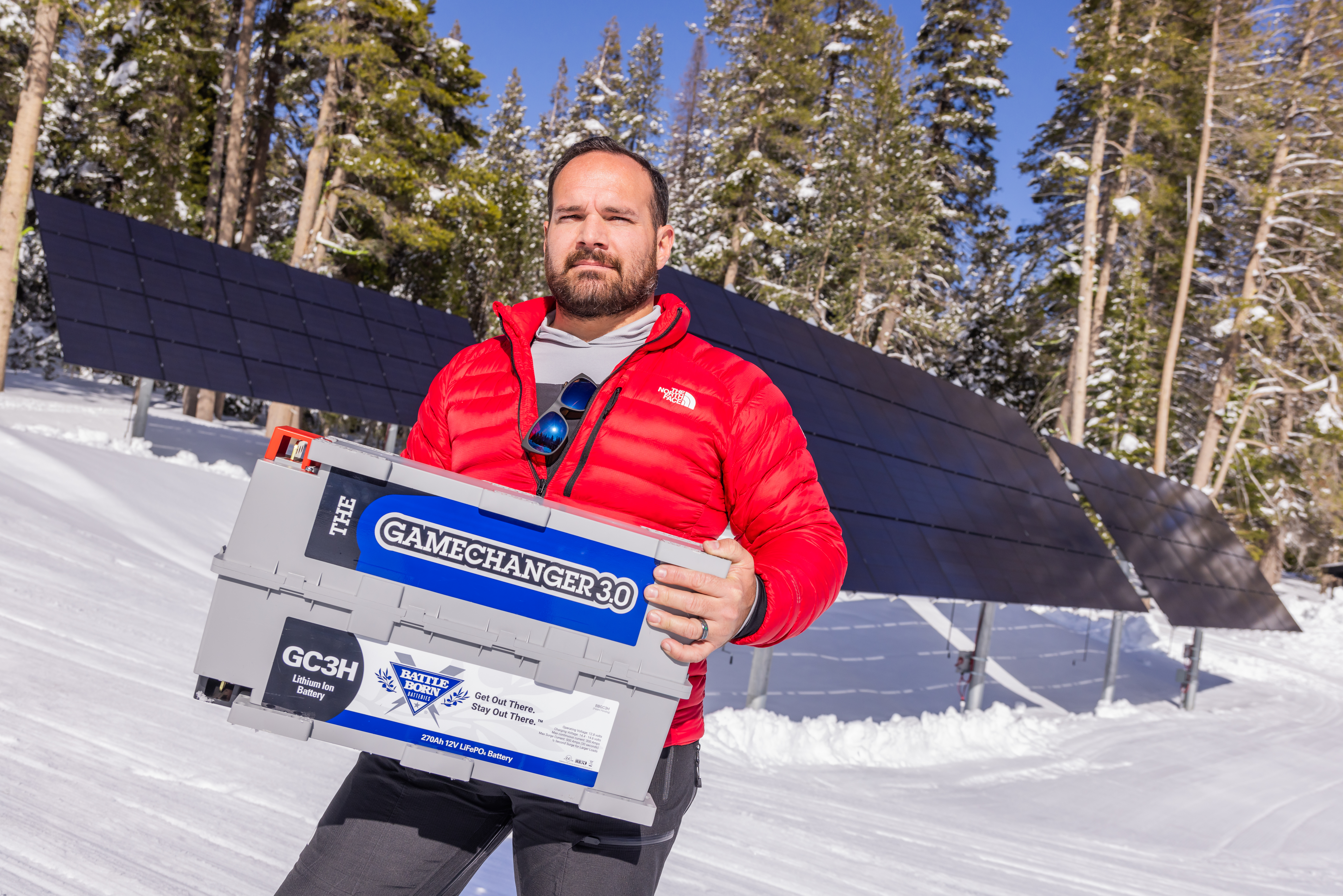 Installer Steven Lewis holding a gc3 battle born batteries in front of solar panels