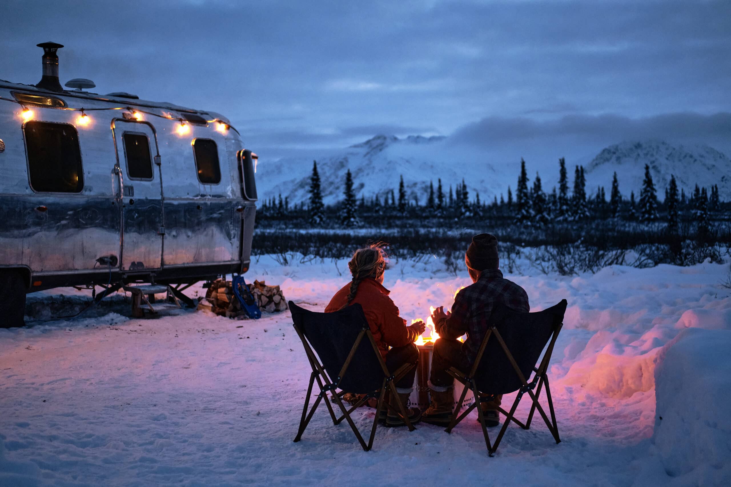 Couple enjoying a fire outside of their RV surrounded by snow